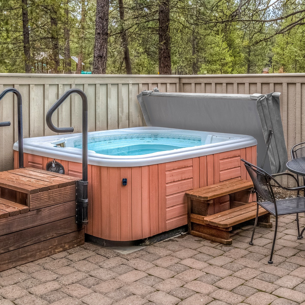 Cubierta gris para jacuzzi de 2,2m x 2,2m, con textura suave, que protege el jacuzzi en un entorno natural y acogedor