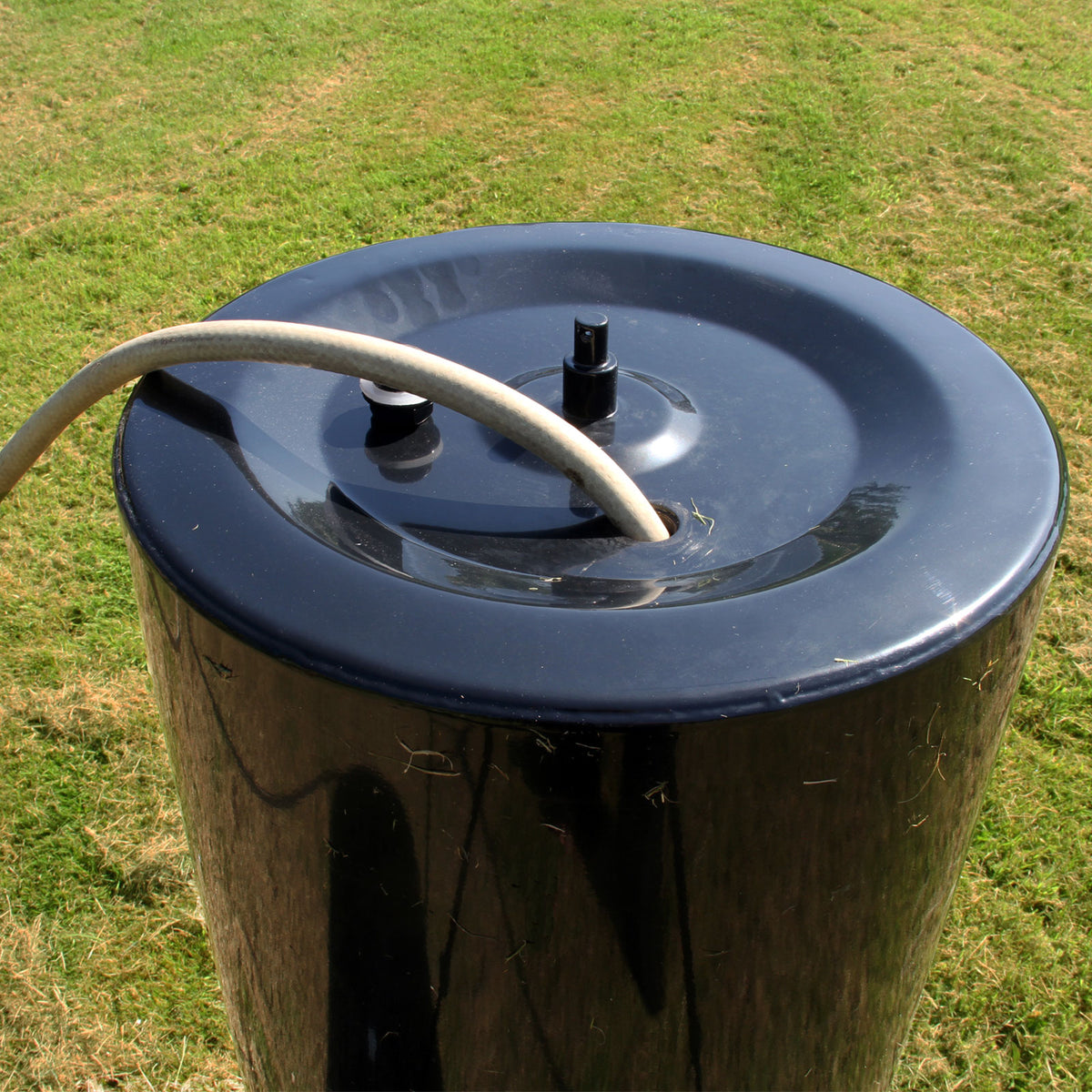 Rodillo de jardín remolcable T-Mech de 120 L, cilindro negro brillante con tapa plana y manguera conectada, sobre césped verde