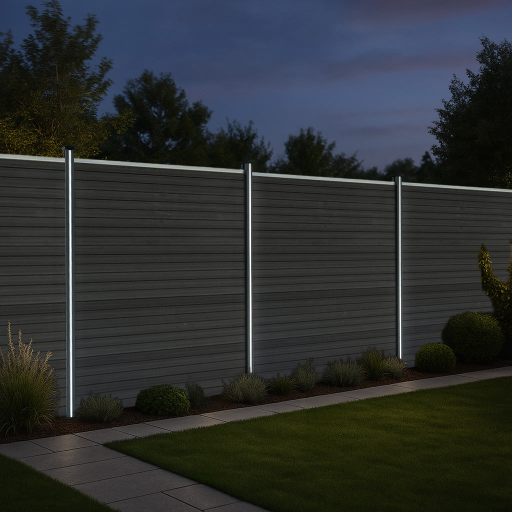 Valla exterior de WPC y aluminio en color gris, con postes iluminados, rodeada de césped y plantas en un ambiente nocturno