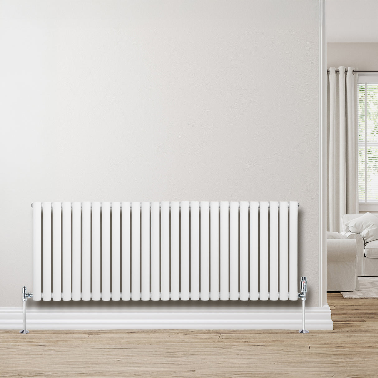Radiador de columna ovalado blanco de 600 mm x 1620 mm, con válvulas, instalado en una pared clara junto a un sofá y ventana