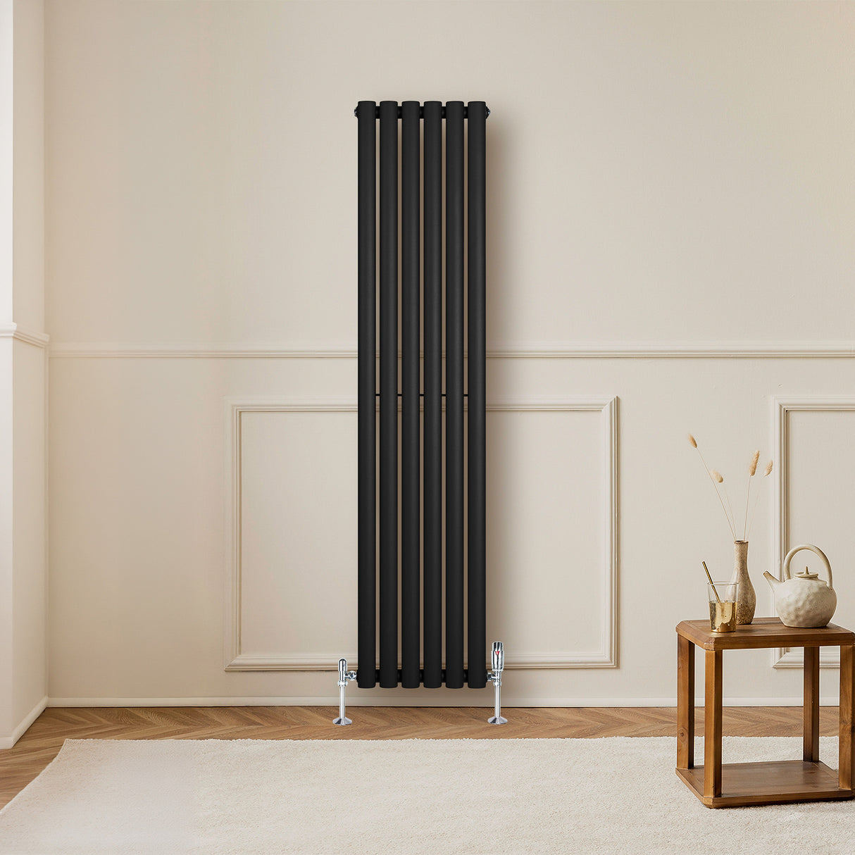 Radiador de columna ovalado negro de 1600 mm x 360 mm con válvulas, instalado en una pared clara, junto a una mesa de madera