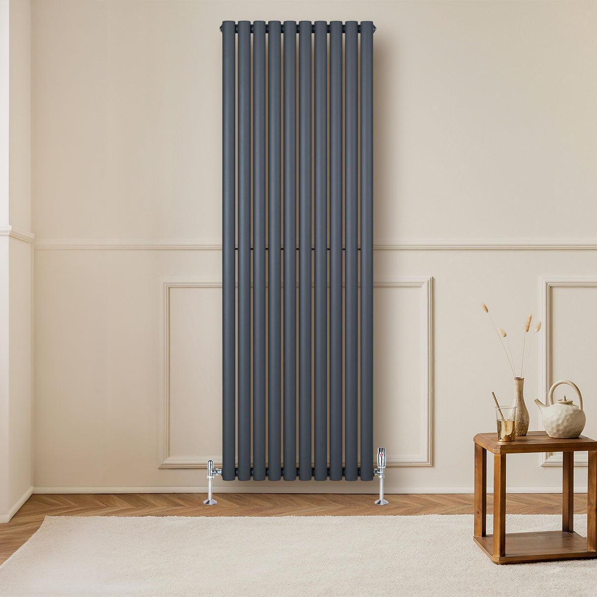 Radiador de columna ovalado en gris antracita, con válvulas, instalado en pared clara, complementando un ambiente moderno y acogedor