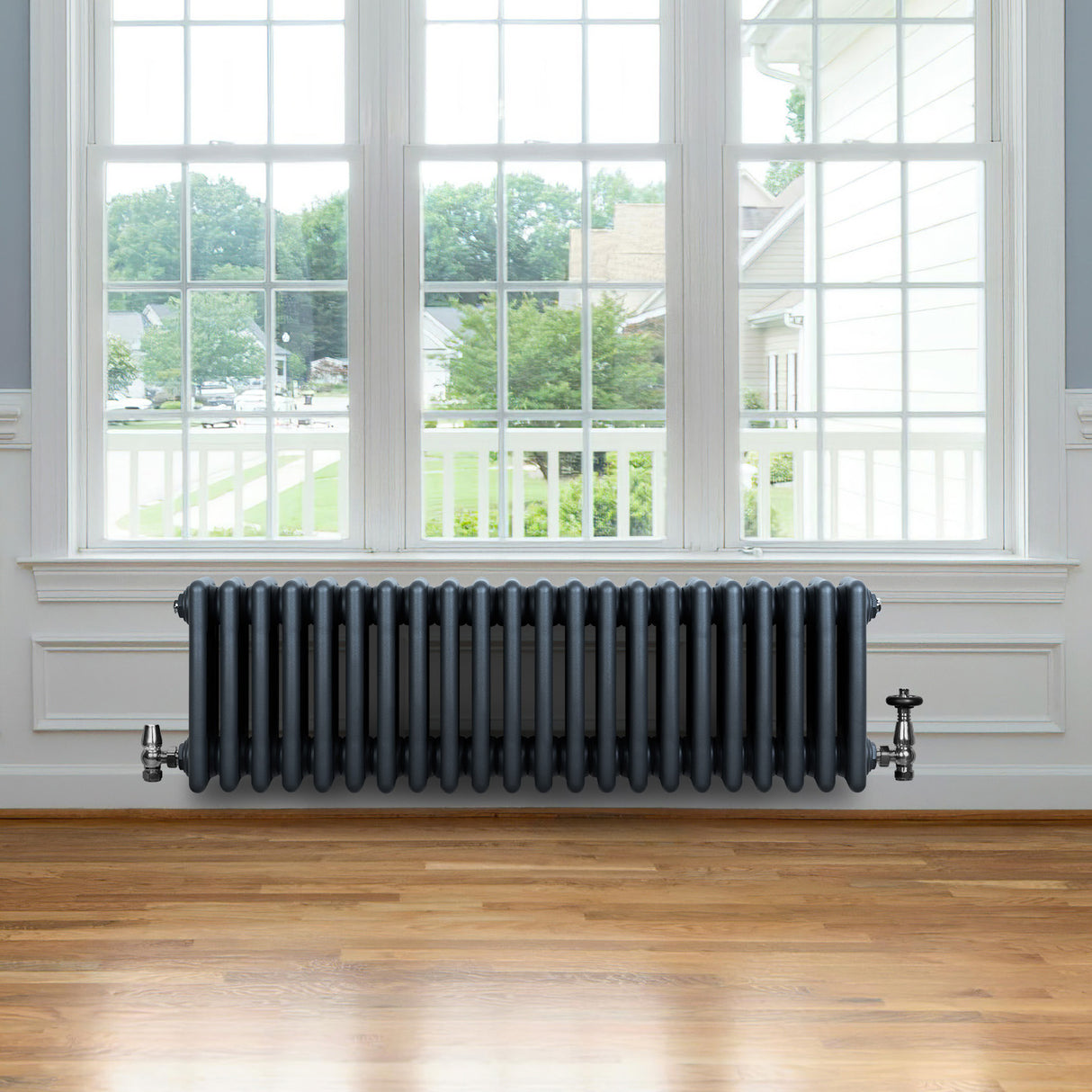 Radiador tradicional de 4 columnas en gris antracita, con válvulas, colocado frente a una ventana en un ambiente luminoso y moderno