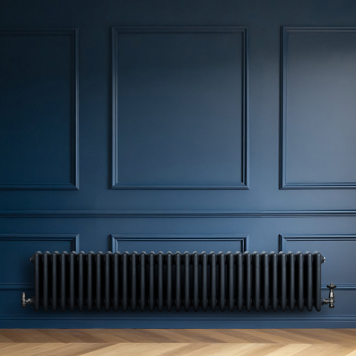 Radiador tradicional de 4 columnas en gris antracita, con válvulas, instalado en una pared azul, sobre un suelo de madera clara