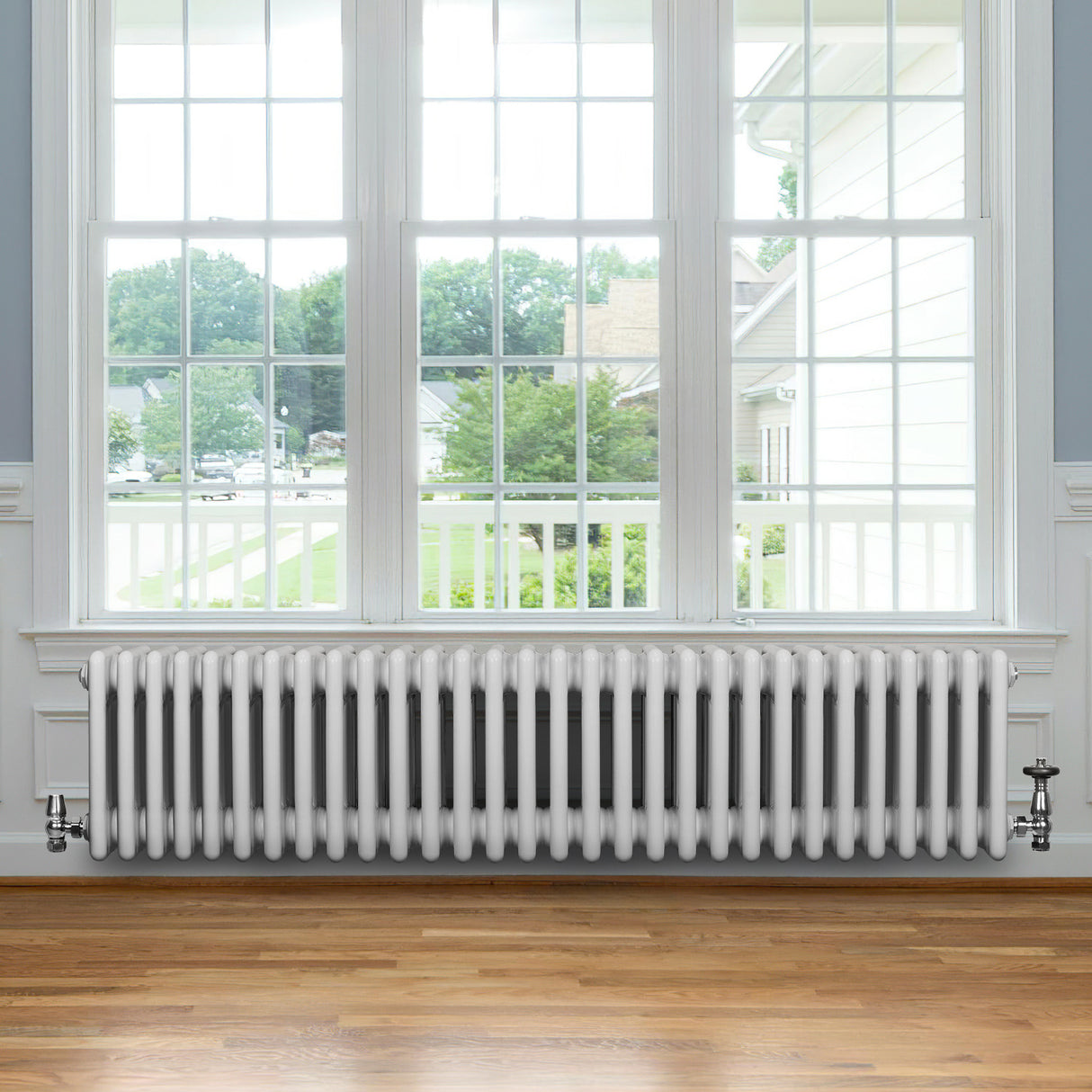 Radiador tradicional de 4 columnas en color blanco, ubicado bajo una ventana, con un diseño elegante y acabado brillante sobre un suelo de madera clara
