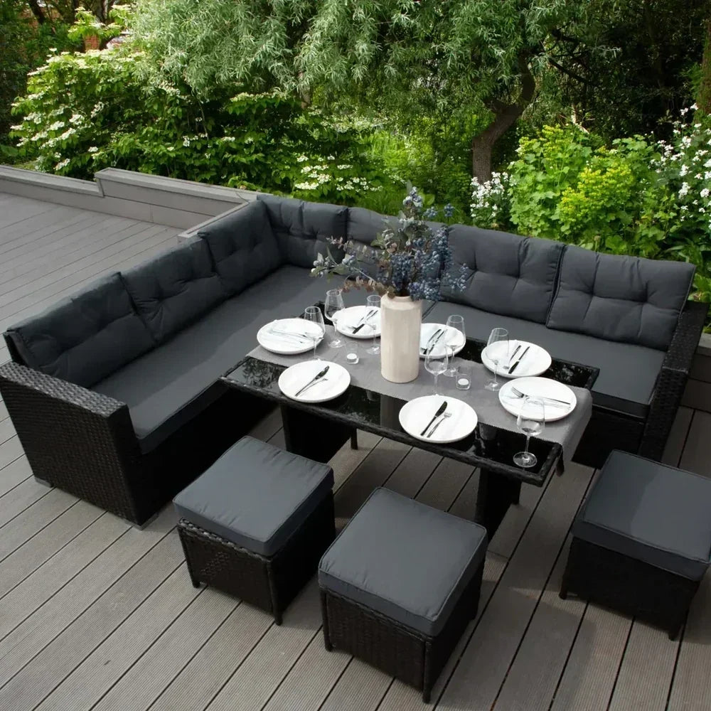 Conjunto de muebles de jardín en tonos oscuros, con cojines grises, mesa negra y platos dispuestos para una comida al aire libre