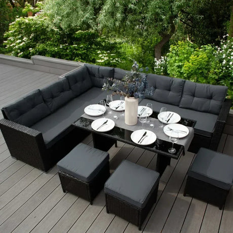 Conjunto de muebles de jardín en tonos oscuros, con cojines grises, mesa negra y platos dispuestos para una comida al aire libre