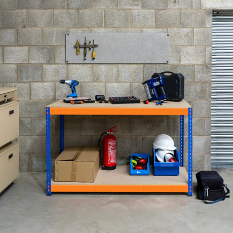 Banco de trabajo azul y naranja con herramientas, cajas de almacenamiento y equipo de seguridad sobre fondo de pared de ladrillo gris
