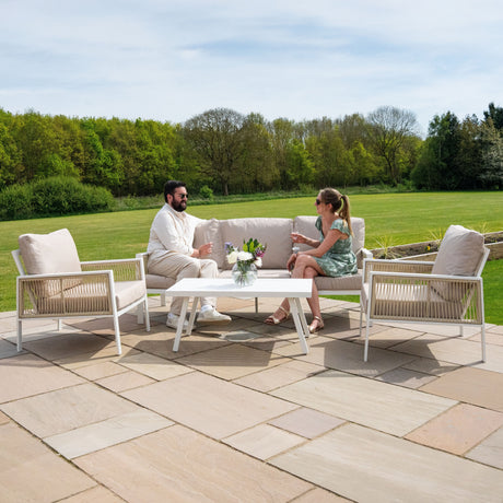 Pareja disfrutando de bebidas en un elegante conjunto de muebles de patio blanco con cojines beige, rodeados de un paisaje verde