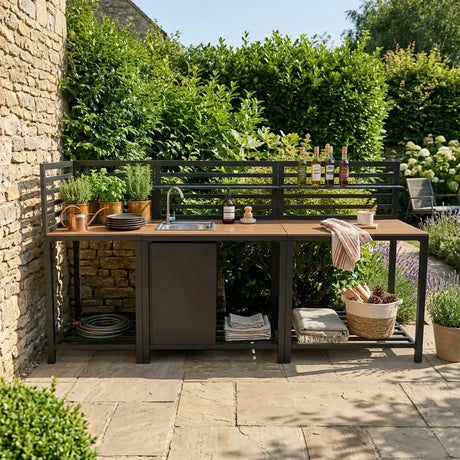 Cocina de exterior moderna con muebles de madera y metal negro, decorada con plantas y utensilios, en un jardín verde y soleado