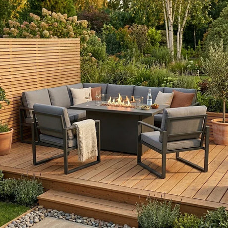 Conjunto de muebles de jardín en tonos grises, con brasero central, rodeado de plantas y madera, ideal para exteriores acogedores