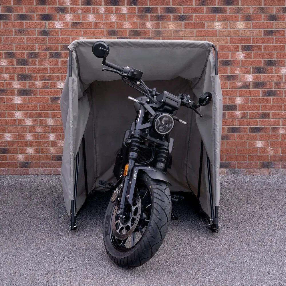 Tienda de moto impermeable en color gris claro, con estructura resistente, protegiendo una motocicleta negra frente a un muro de ladrillos