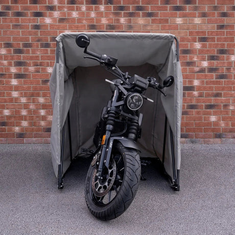 Tienda de moto impermeable en color gris claro, con estructura resistente, protegiendo una motocicleta negra frente a un muro de ladrillos