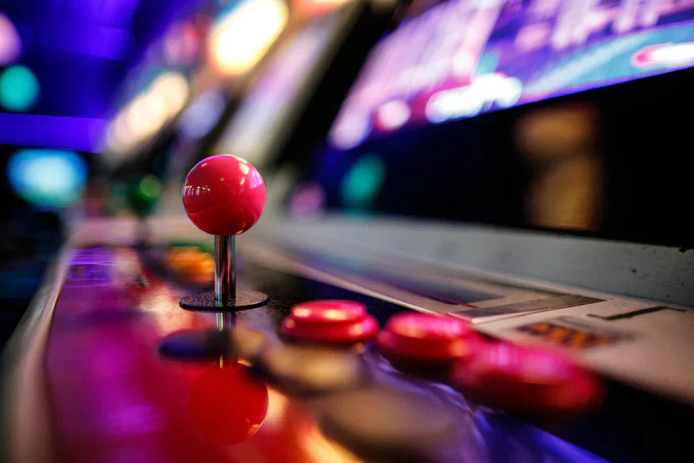 Palanca de arcade rosa brillante y botones coloridos en una máquina retro, con fondo iluminado en tonos morados y azules
