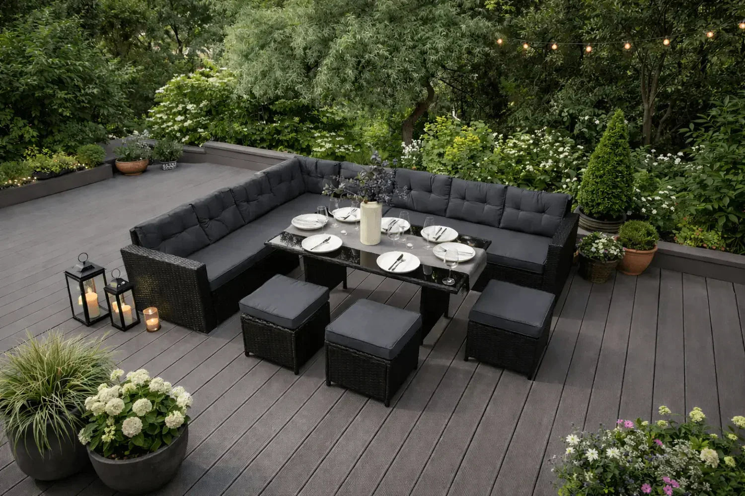 Conjunto de muebles de jardín en tonos oscuros, con mesa de vidrio y sillas acolchadas, rodeado de plantas y luces decorativas