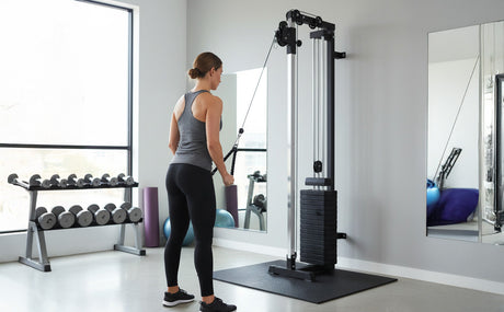 Mujer entrenando con máquina de cable de polea negra en un gimnasio moderno, con espejos y pesas en el fondo