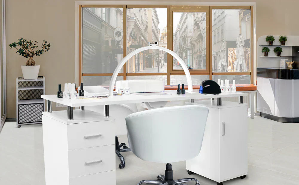 Mesa de manicura blanca moderna con sillas ergonómicas, productos de belleza organizados y luz natural que entra por las ventanas