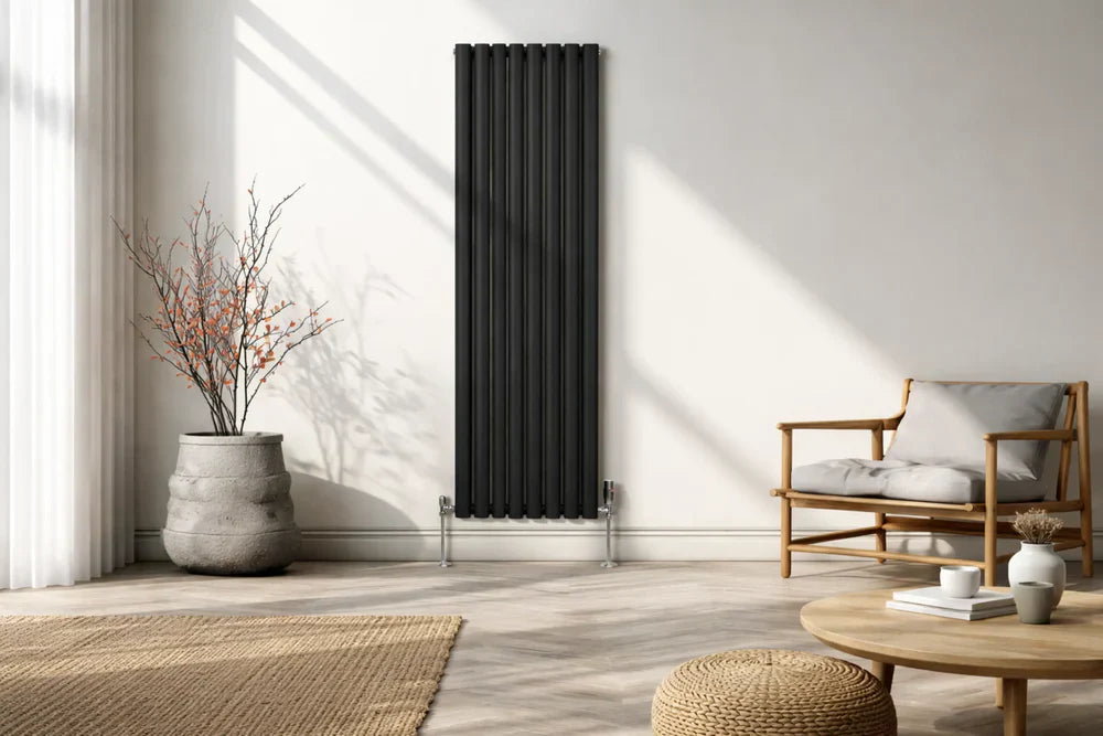 Radiador de columnas negro en una pared blanca, junto a una planta en maceta y un sillón de madera en un ambiente moderno y acogedor
