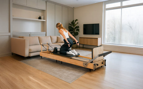 Mujer realizando ejercicios en un reformador de pilates de madera clara, en una sala moderna con luz natural y muebles neutros