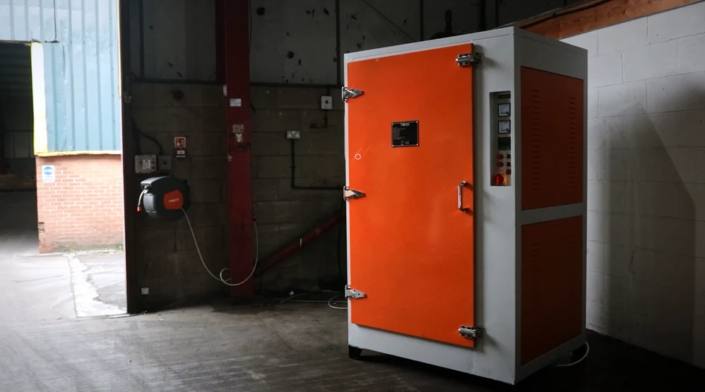Horno de pintura en polvo de color naranja y blanco, con puerta cerrada y panel de control visible, ubicado en un taller industrial