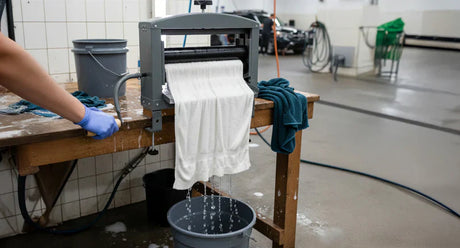 Escurridor manual en acción, con ropa blanca goteando agua, fondo de taller con herramientas y superficies limpias y brillantes