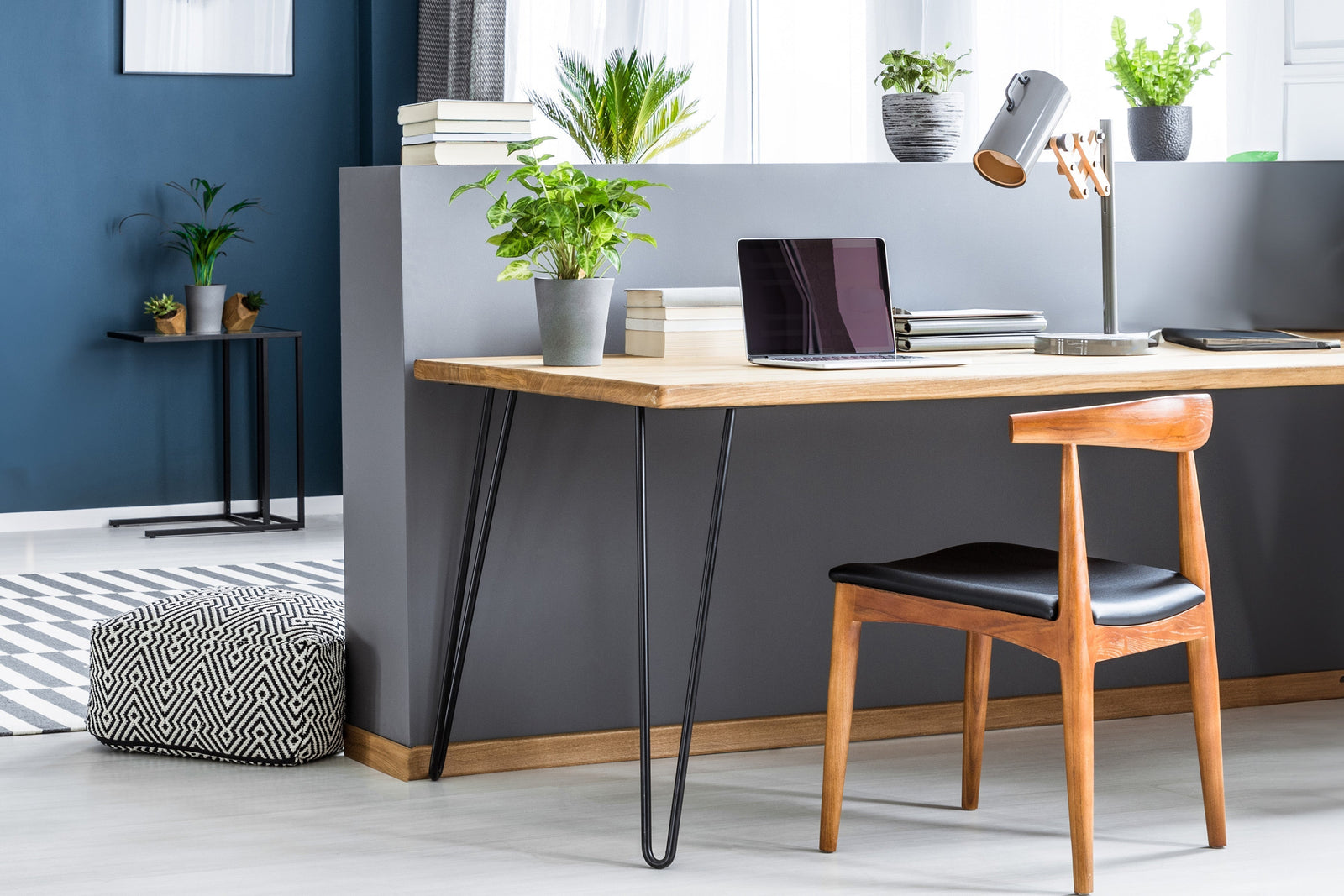 Mesa de madera clara con patas de horquilla negras, silla de madera con asiento negro, plantas decorativas y laptop sobre la mesa