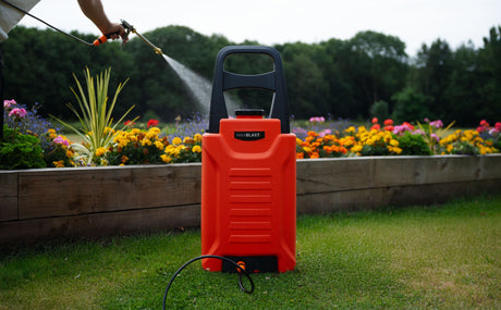 Rociador portátil naranja sobre césped verde, rodeado de flores coloridas, ideal para jardines sin enredos ni pesadez