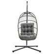Silla colgante tipo huevo de ratán gris con cojín acolchado, estructura metálica negra y diseño moderno y elegante