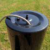 Rodillo de jardín remolcable T-Mech de 120 L, cilindro negro brillante con tapa plana y manguera conectada, sobre césped verde