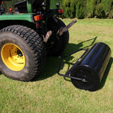 Rodillo de jardín remolcable T-Mech de 120 L, cilindro negro brillante con marco metálico, acoplado a un tractor en césped verde