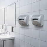 Secadores de manos comerciales MAXBLAST en acabado plateado, instalados en una pared blanca de azulejos, junto a un lavabo moderno