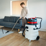 Aspirador industrial de sólidos y líquidos de 90 L, con manguera y boquilla, en un ambiente moderno con sofá gris y suelo de madera clara
