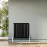 Radiador de columna ovalado negro de 600 mm x 600 mm, con válvulas, instalado en una pared clara junto a un ventanal