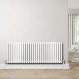 Radiador de columna ovalado blanco de 600 mm x 1620 mm, con válvulas, instalado en una pared clara junto a un sofá y ventana