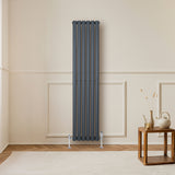 Radiador de columna ovalado en gris antracita, con válvulas, instalado en pared clara, junto a una mesa de madera y decoración minimalista