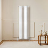 Radiador de columna ovalado blanco de 1600 mm x 480 mm, con válvulas, instalado en una pared clara junto a una mesa de madera