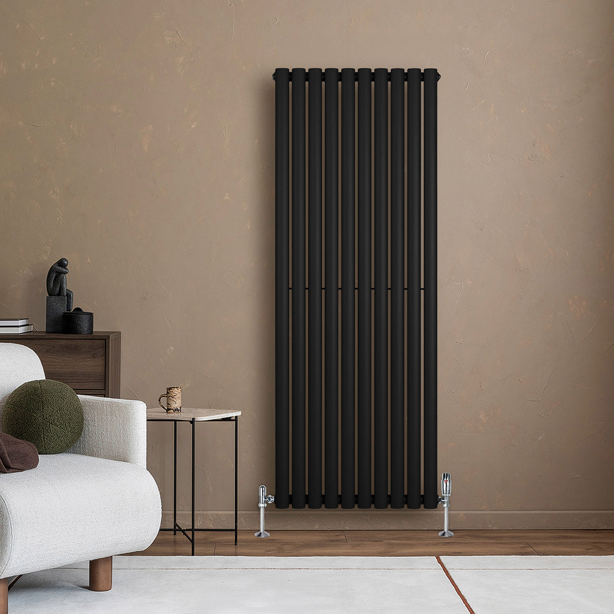 Radiador de columna ovalado negro de 1600 mm x 600 mm, con válvulas, instalado en una pared de color claro, junto a un sofá moderno