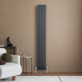 Radiador de columna ovalado en gris antracita, con válvulas, instalado en pared beige, junto a mesa y sofá moderno