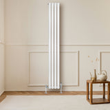 Radiador de columna ovalado blanco de 1800 mm x 240 mm, con válvulas, instalado en una pared clara junto a una mesa de madera
