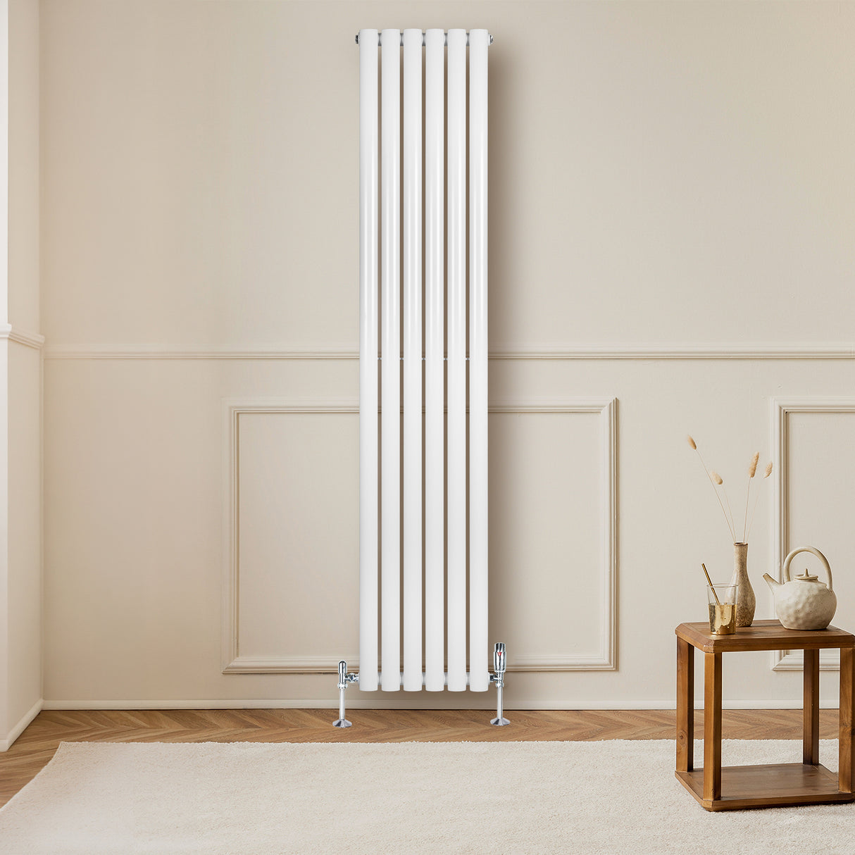 Radiador de columna ovalado en blanco, con diseño vertical y válvulas, instalado en una pared clara, junto a una mesa de madera
