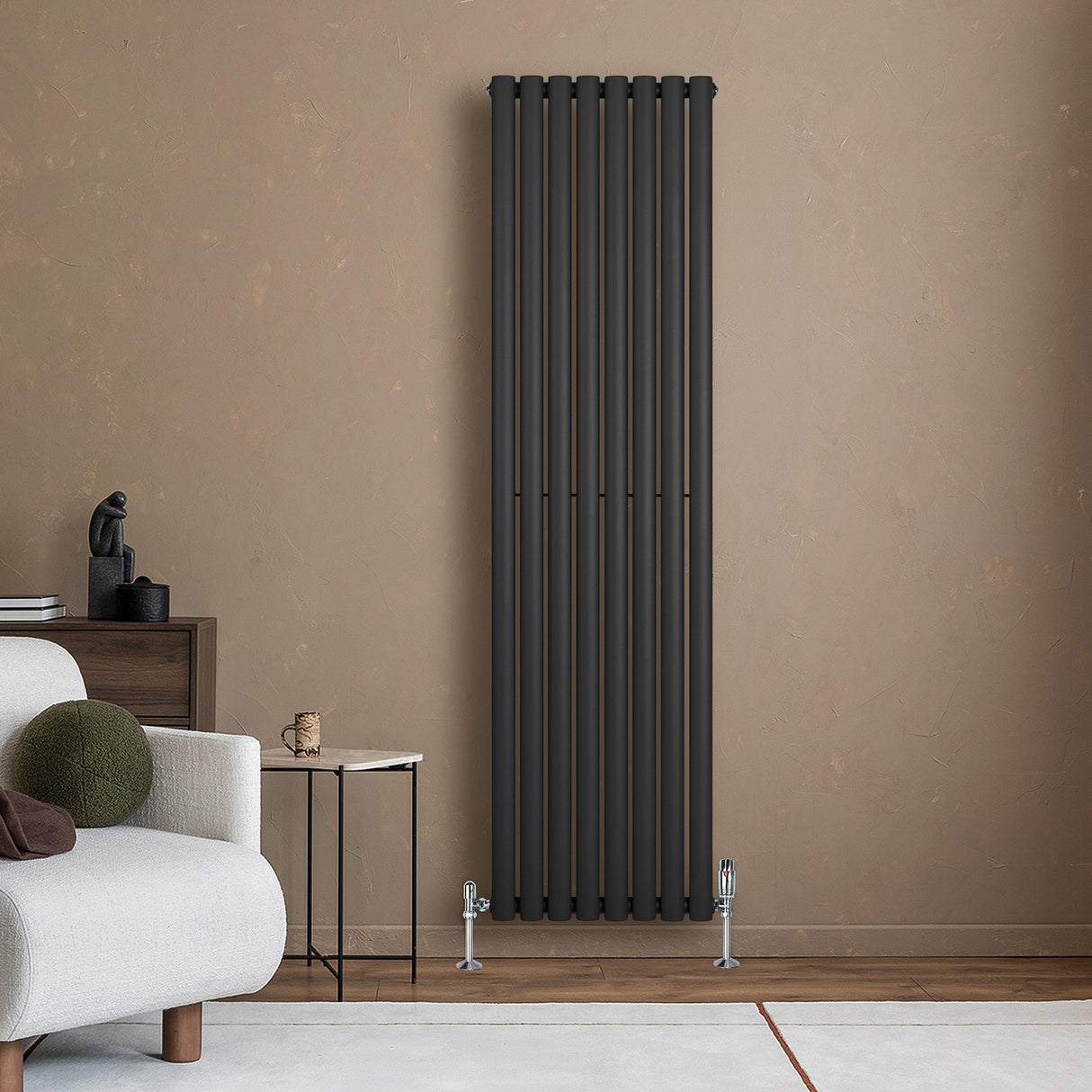 Radiador de columna ovalado negro de 1800 mm x 480 mm, con válvulas, instalado junto a un sofá en un ambiente moderno y cálido