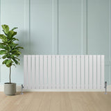Radiador plano de columna simple blanco de 600 x 1400 mm, con válvulas, colocado junto a una planta en maceta sobre un suelo de madera clara