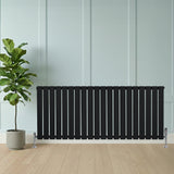 Radiador plano de columna simple negro de 600 x 1400 mm, con válvulas, ubicado junto a una planta en maceta sobre un suelo de madera clara