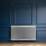 Radiador tradicional de 4 columnas en color blanco, con válvulas, instalado en una pared azul, destacando su diseño elegante y moderno