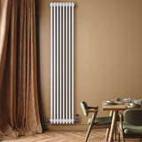 Radiador tradicional de 4 columnas en color blanco, instalado en una pared marrón, junto a una mesa de comedor elegante y moderna