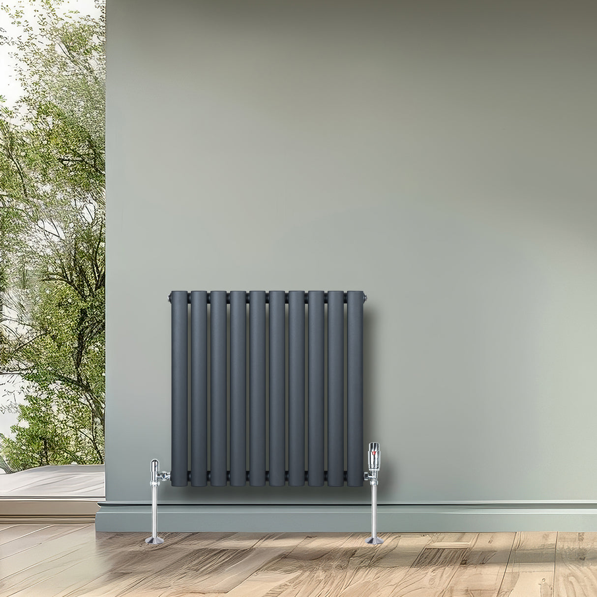 Radiador de columna ovalado gris antracita, con válvulas, instalado en una pared verde, sobre un suelo de madera clara