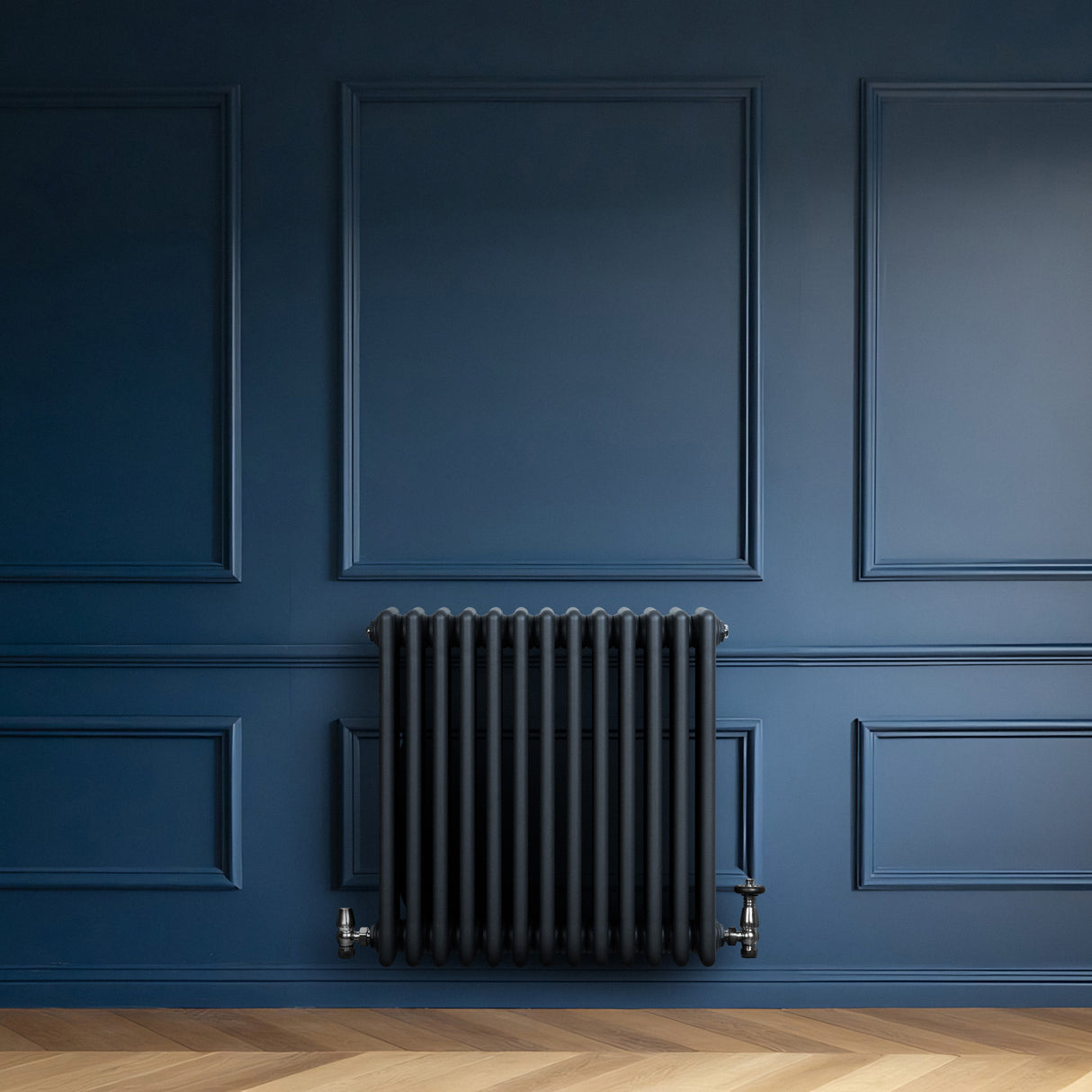 Radiador tradicional de 4 columnas en gris antracita, con acabado mate, instalado en una pared azul oscuro, complementando el ambiente elegante