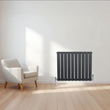 Radiador de columna única en gris antracita, con diseño moderno y elegante, colocado junto a un sillón en un ambiente luminoso