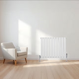 Radiador de columna única blanco de 600 mm x 700 mm, con diseño moderno y acabado liso, colocado junto a un sillón en un ambiente luminoso