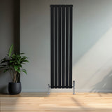 Radiador de columna única negro de 1600 mm x 420 mm, con diseño vertical y acabado liso, instalado en una pared clara junto a una planta decorativa